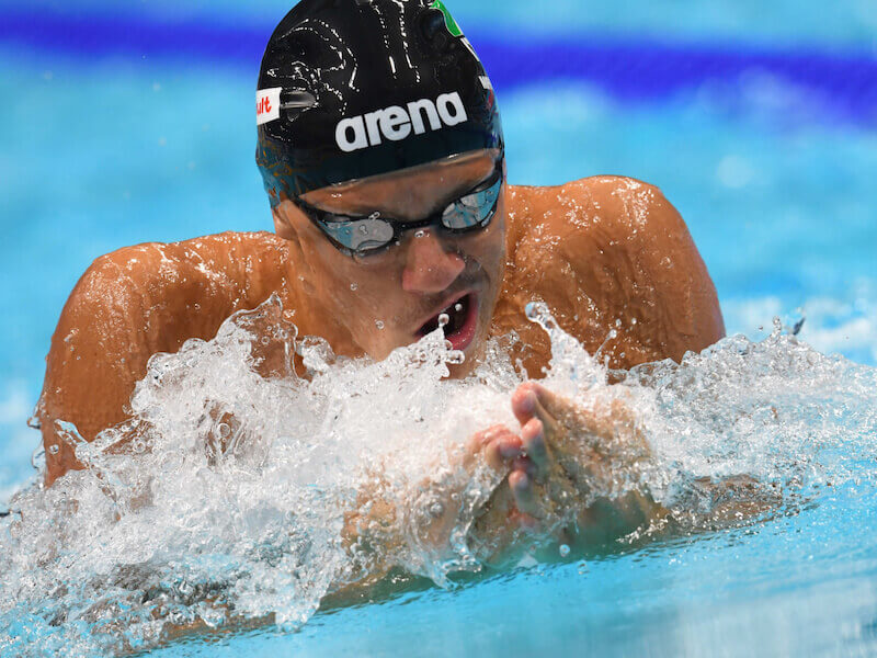 A closeup of a man wearing an arena swim cap and doing the breaststroke