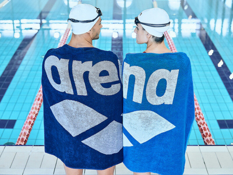 Getting back into swimming: Two swimmers wrapped in arena towels stand by the edge of a pool