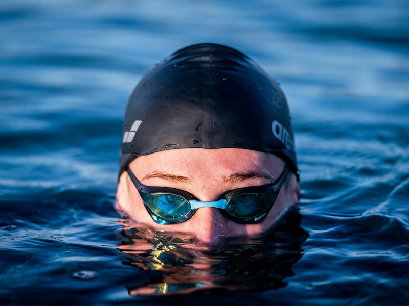 A swimmer brings the top of his head out of the water while using nose plugs for swimming