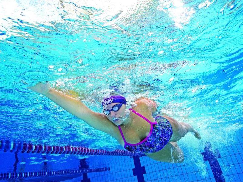 Swimming warm up sets: underwater shot of a swimmer wearing googles, swim cap and swimsuit