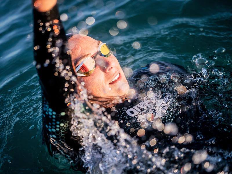 Swimmer wearing an open water swimming wetsuit raising her hand while in the water