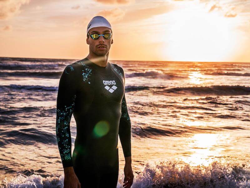 Swimmer wearing an open water swimming wetsuit standing near the sea