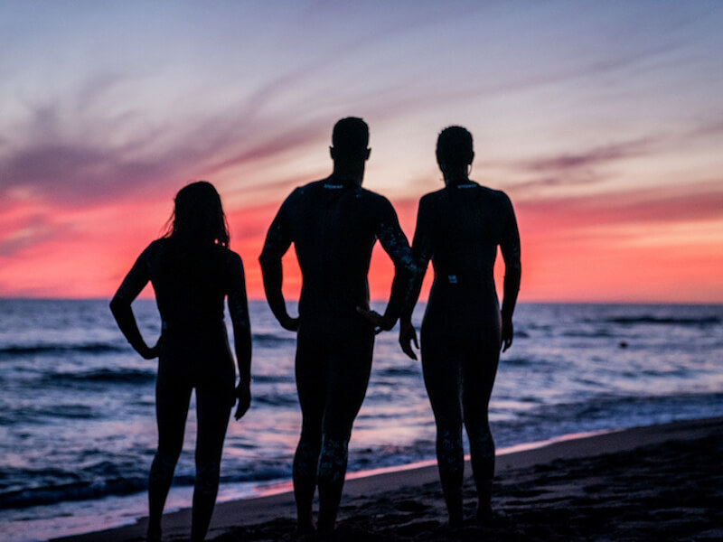 Open water swimming gear: 3 people standing on a beach